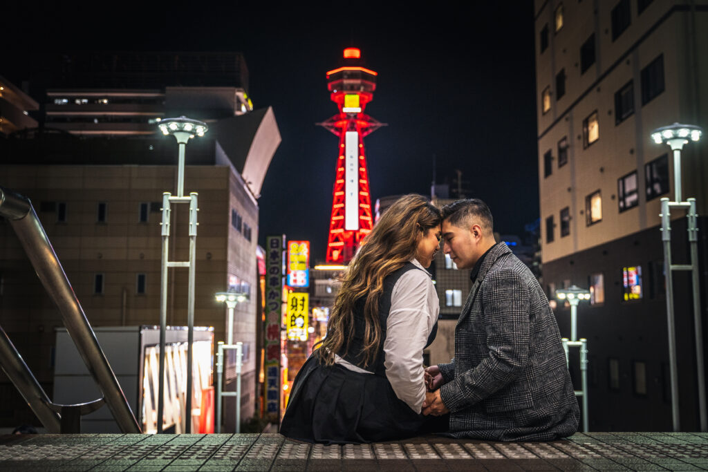 couple sitting and looking at each other with Tsutenkaku Tower in the background