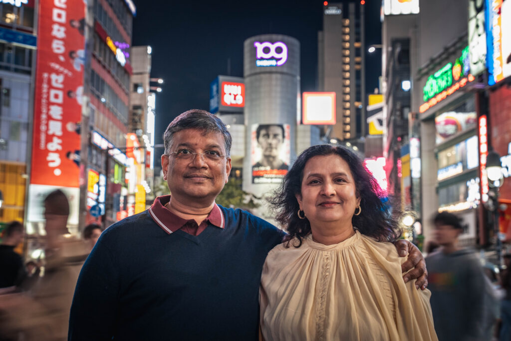 couple with man holding his partner's shoulder looking at the camera at Shibuya Crossing Tokyo