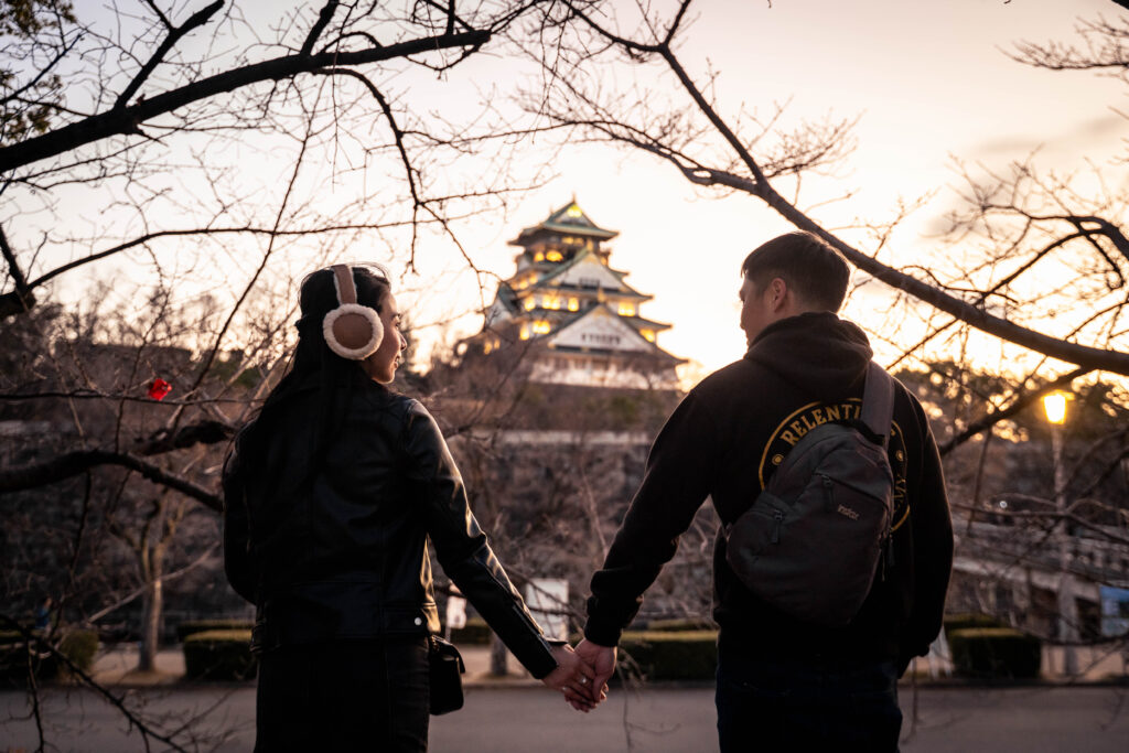 couple holding hands looking toward Osaka Castle at sunset